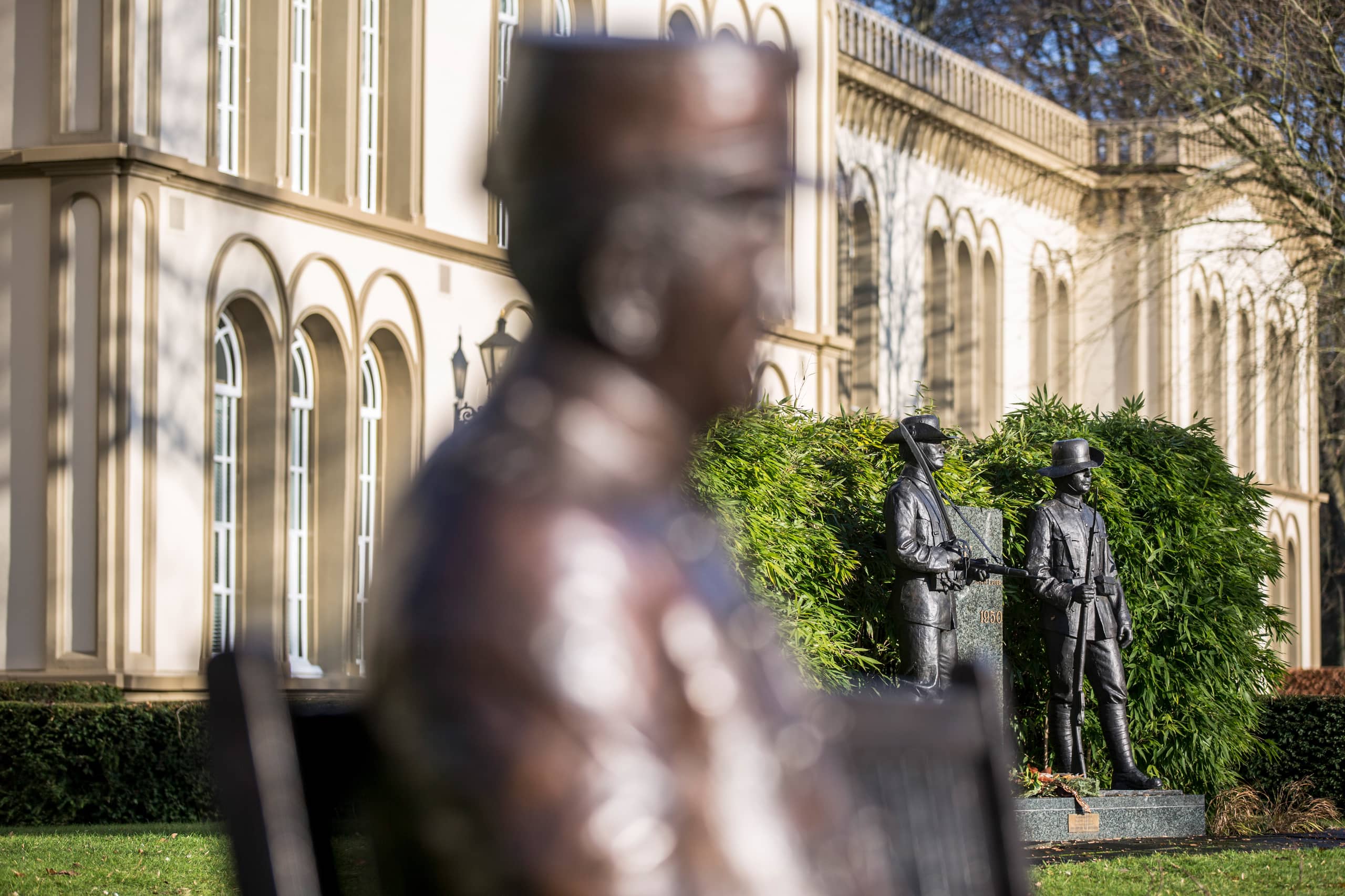 Zicht op het KNIL-monument op het landgoed Bronbeek, met op de voorgrond het bankje waarop de in brons gegoten KNIL-soldaat Jan Bronbeek zit.