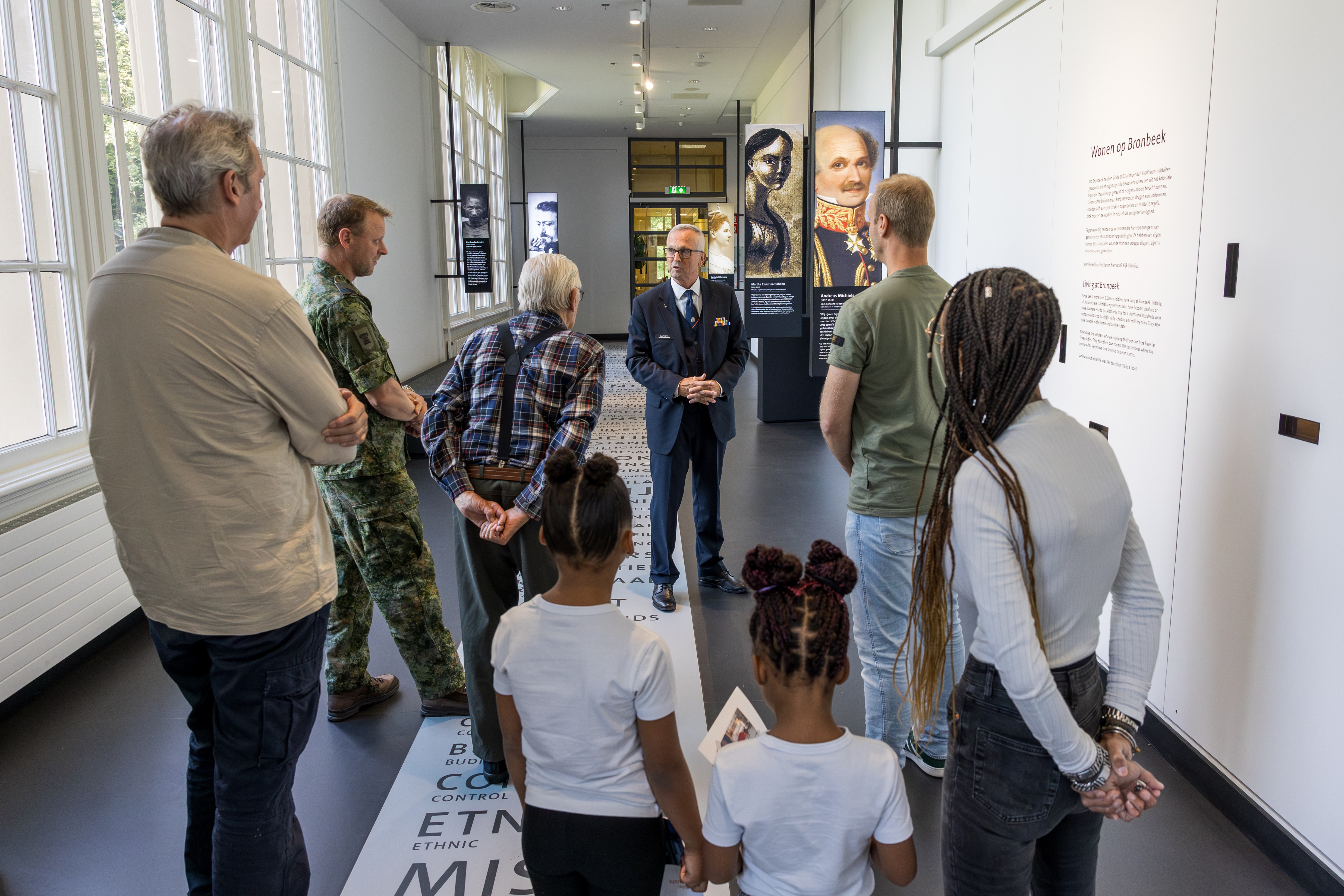 Rondleiding door een gids in museum Bronbeek, met op de foto een gezin met twee jonge kinderen een militair, een bewoner van Bronbeek en hoofd Museum.